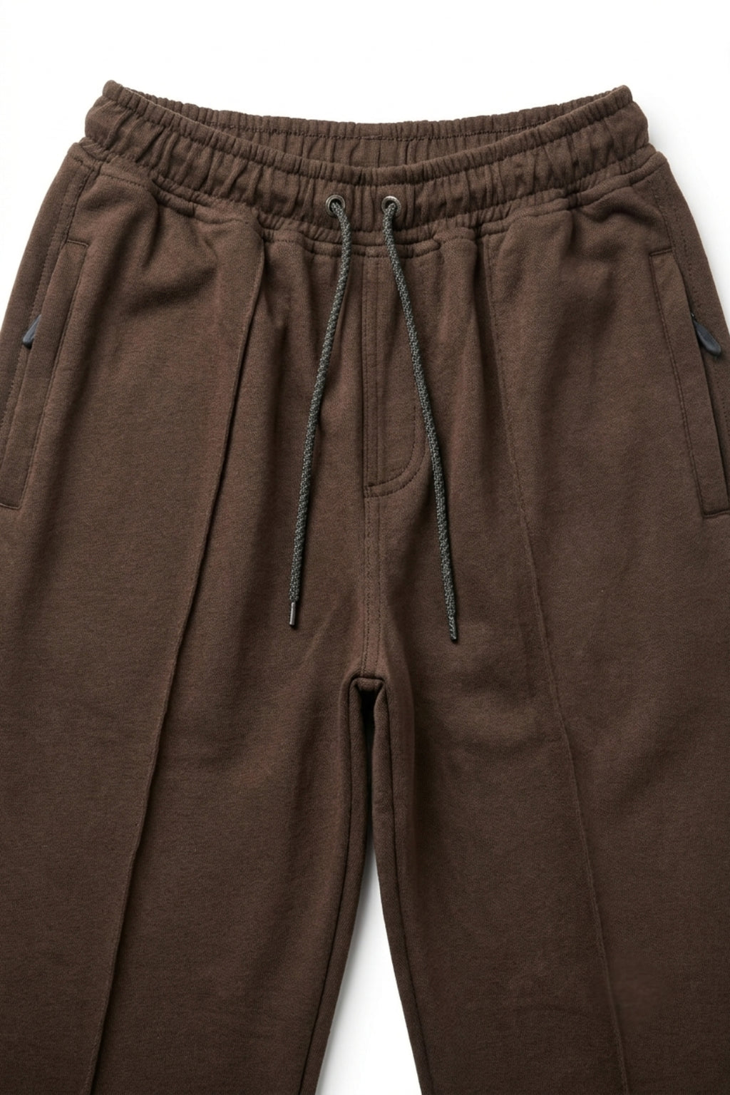 Close-up of dark brown terry trousers showing the elastic waistband, adjustable drawstrings, and integrated zippered side pockets.