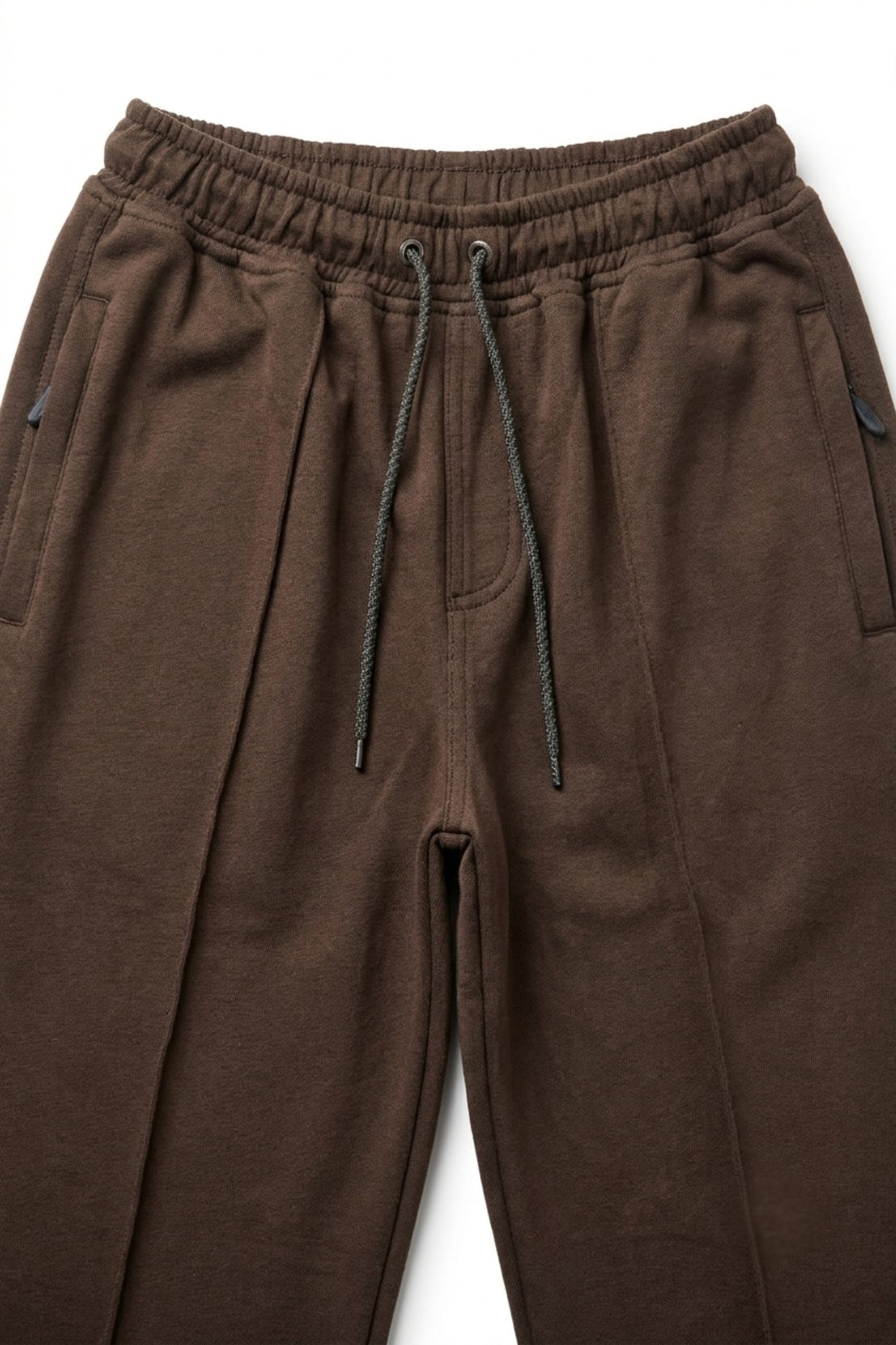 Close-up of dark brown terry trousers showing the elastic waistband, adjustable drawstrings, and integrated zippered side pockets.