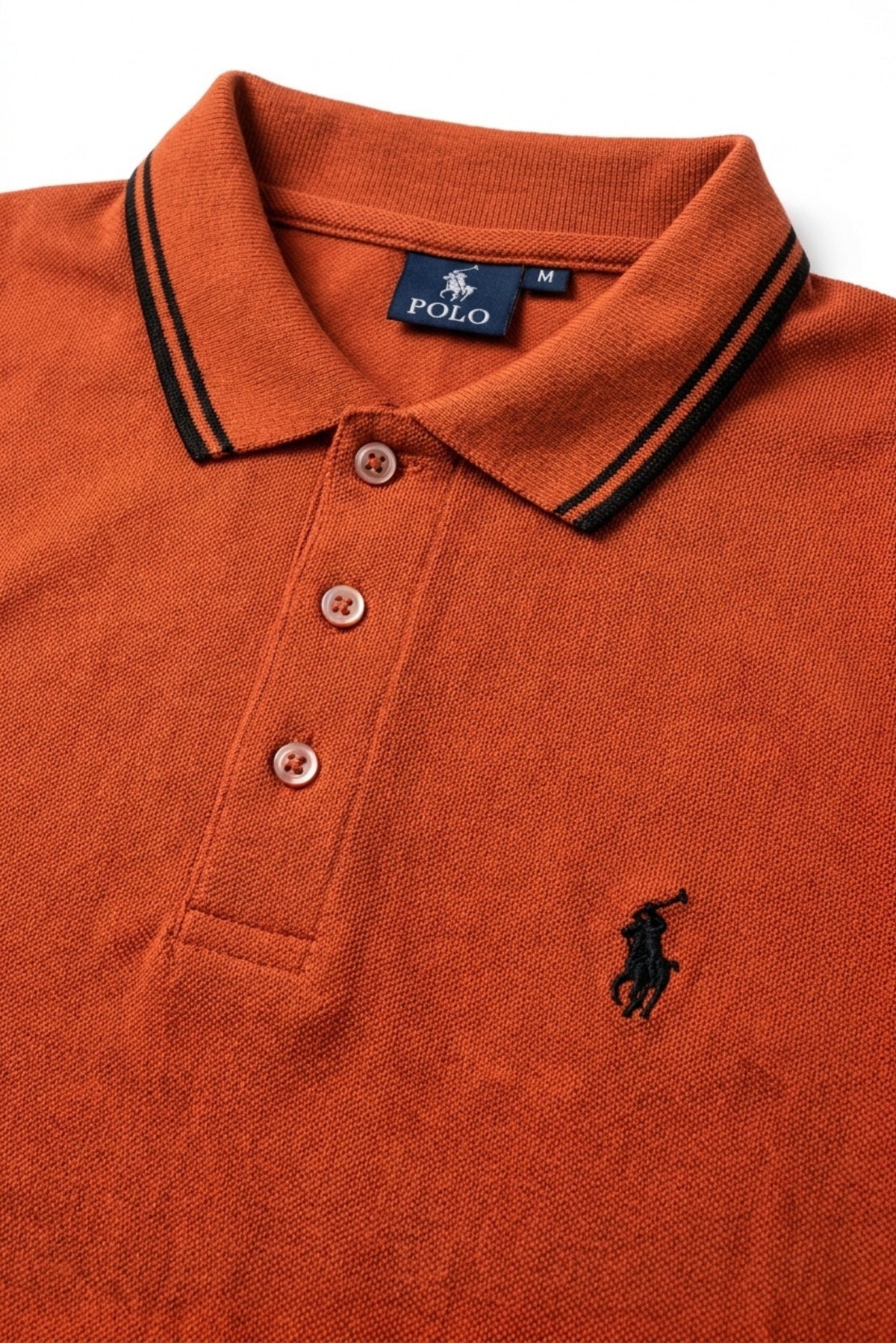 Close-up detail of Eliteez Piqué Polo Rider Rust Orange embroidered logo