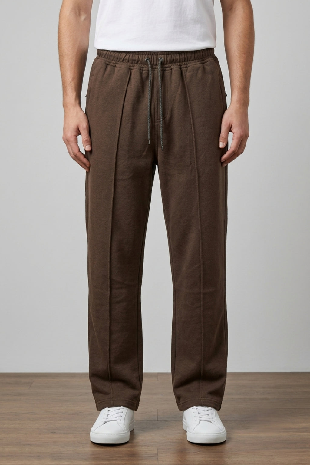 A man wearing Classic Lounge Lightweight Terry Trousers in dark brown, featuring a relaxed wide-leg fit and tucked-in white t-shirt, standing in a studio.